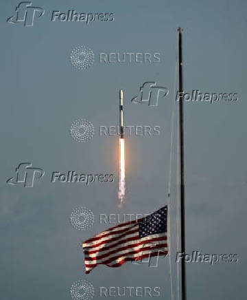 An American flag flies at half staff in honor of former President Jimmy Carter at the Kennedy Space Center press site as a SpaceX Falcon 9 rocket lifts off from the Cape Canaveral Space Force Station