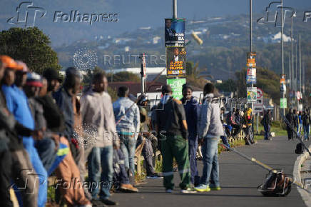 Job seekers sit beneath campaign posters for the South African general elections, in Cape Town