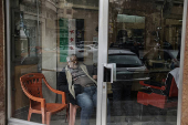 Man sits next to the flag adopted by the new Syrian rulers inside his shop in Damascus