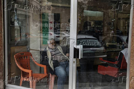 Man sits next to the flag adopted by the new Syrian rulers inside his shop in Damascus