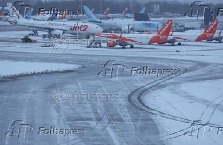 Staff use a tractor to help clear snow from around aircraft after overnight snowfall caused the temporary closure of Manchester Airport, in Manchester