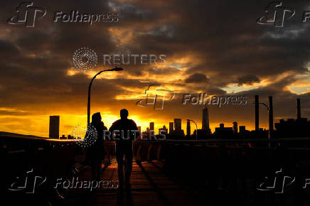 The sun sets behind the Lower Manhattan skyline in the Brooklyn borough of New York City