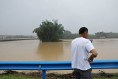 Resident uses his phone as he stands near a flooded river following heavy rainfall in Qingyuan