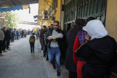 A man holds a stack of bread as people queue to receive bread outside a bakery in Aleppo