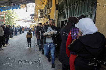 A man holds a stack of bread as people queue to receive bread outside a bakery in Aleppo