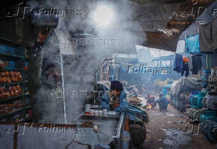 People sit next to a fire at a market area on a cold winter morning in the old quarters of Delhi