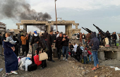 Smoke rises from the Syrian side, as people gather with belongings at the damaged site on the Lebanese-Syrian border crossing of Arida