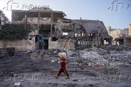 A boy carrying stacks of bread on his head walks past a damaged school in Aleppo