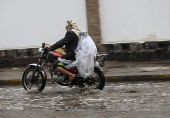 Boy is covered with a plastic bag as he rides a motorcycle during rains in Sanaa