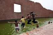 Children jump into the water body of Martyred Intellectuals Memorial at Rayerbazar, to cool themselves during a heatwave in Dhaka