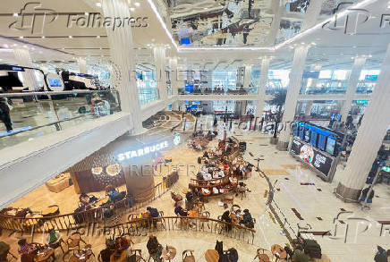 People sit at a coffee shop as they wait for their flight after a rainstorm hits Dubai, causing delays at the Dubai International Airport