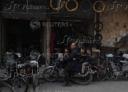 Children sit on a motorcycle with their relative, in Douma