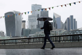 FILE PHOTO: A pedestrian carrying an umbrella walks along the River Thames in view of City of London skyline in London