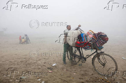 A vendor selling bedsheets loads them onto his bicycle on a foggy and cold winter morning in New Delhi