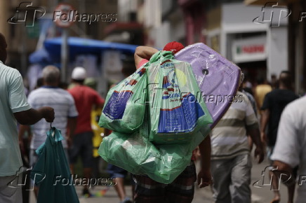 Homem carrega sacolas durante compras na 25 de Maro em SP