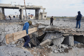 People stand near a damaged site at the Lebanese-Syrian border crossing of Arida