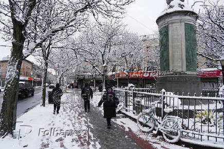 People walk along the sidewalk during the city's first snowfall of the season, on the first day of winter in the Queens borough of New York City