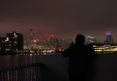 A man watches the Canary Wharf skyline from the Royal Docks during foggy weather in London