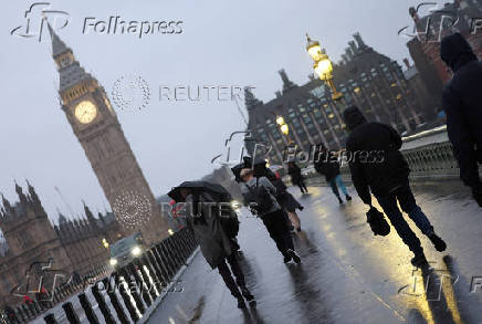 People shield from rain during morning rush-hour near Houses of Parliament, in London