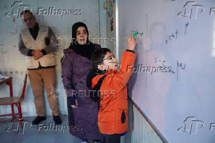 A student writes on a board inside a portable classroom in Aleppo