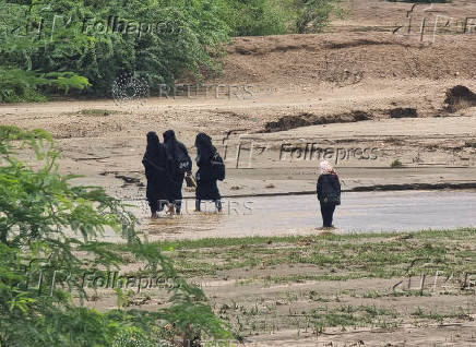 Women walk through flood water following heavy rains in Hajjah