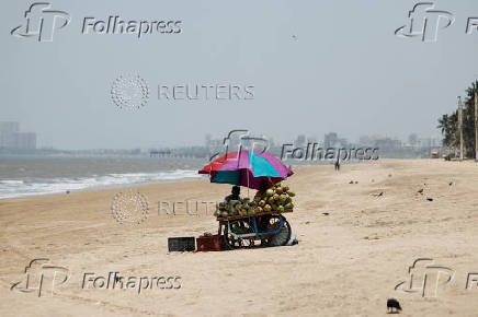 Vendor selling coconut water waits for customers at a beach on a hot day in Mumbai