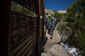 Asylum seeking migrants climb past the border wall into the United States from Mexico