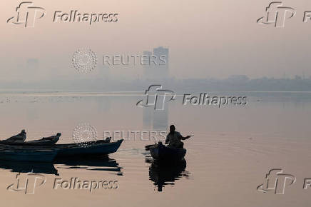 A fisherman is silhouetted as he rows a boat amid smog and air pollution on a morning in Karachi