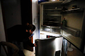 A woman looks inside of a fridge in a damaged neighbourhood near the Israel-Lebanon borderin Manara