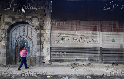 A girl holds her sibling along the street, in Douma