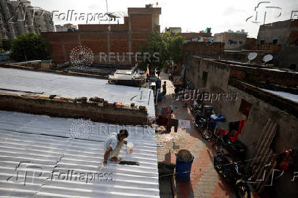 A painter applies solar reflective paint on roofs in a slum area in Ahmedabad