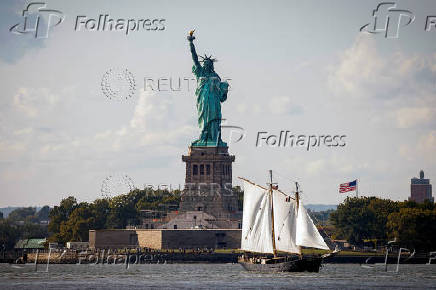 A sailboat passes by the Statue of Liberty in New York Harbor, in New York