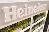 Bottles of Heineken beer are displayed on a shelf in a supermarket