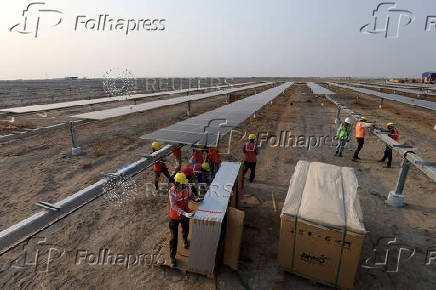 Workers install solar panels at the Khavda Renewable Energy Park of Adani Green Energy Ltd (AGEL), in Khavda