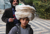 A boy walks with stacks of bread on his head, in Damascus