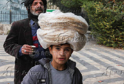 A boy walks with stacks of bread on his head, in Damascus