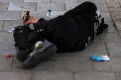 A man lies on a sidewalk with a cup for spare change near a bus stop in Tel Aviv, Israel