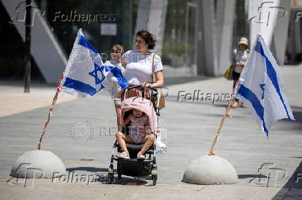 A woman with children walks past Israeli flags in Tel Aviv