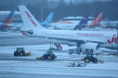 Staff use tractors to help clear snow from around aircraft after overnight snowfall caused the temporary closure of Manchester Airport in Manchester