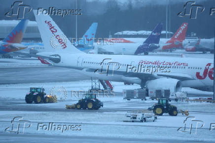 Staff use tractors to help clear snow from around aircraft after overnight snowfall caused the temporary closure of Manchester Airport in Manchester