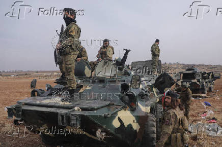 Rebel fighters stand on a military vehicle in Homs countryside