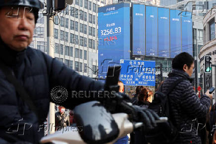 Pedestrians wait for a street signal on a sidewalk as an electronic billboard shows the Shenzhen stock index in Shanghai