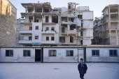 A boy walks near portable classrooms set up in a damaged school yard in Aleppo