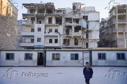 A boy walks near portable classrooms set up in a damaged school yard in Aleppo