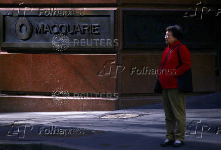 FILE PHOTO: A pedestrian stands near the logo of Australia's biggest investment bank Macquarie Group Ltd which adorns a wall on the outside of their Sydney office headquarters in central Sydney, Australia