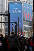 Pedestrians wait for a street signal on a sidewalk as an electronic billboard shows the Shenzhen stock index in Shanghai