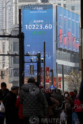 Pedestrians wait for a street signal on a sidewalk as an electronic billboard shows the Shenzhen stock index in Shanghai