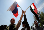 FILE PHOTO: A Russian soldier waves flag with a Syrian woman during the re-opening of the road between Homs and Hama in Rastan