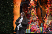 A woman smiles for a photo as she stands in front of a Christmas window display outside Selfridges, on Oxford Street in London