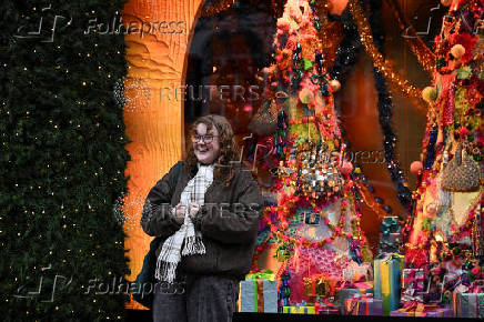 A woman smiles for a photo as she stands in front of a Christmas window display outside Selfridges, on Oxford Street in London